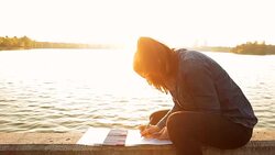 Beautiful young woman coloring books on the lake shore at sunset - Brief 603439111 ï¿½CreativeContentBriefï¿½ Stock Footage
