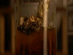 Gold foil dipped into clear orange solution, fizzing as nitrogen dioxide is released and gold disappears, (sound available) Stock Footage