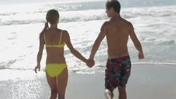 Young couple holding hands and running from beach into surf Stock Footage