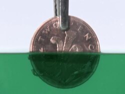 2 pence piece being put into a solution that removes the copper, turning it silver Stock Footage