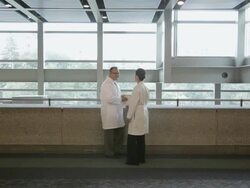 WS Physician standing in hospital corridor looking at a patient chart and greeted by a female colleague / Seattle, Washington, USA Stock Footage