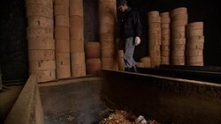 A factory worker carries away a wooden cask stored next to a smoky pit. Stock Footage