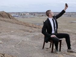 MS Young businessman dressed in black suit trying to get reception for his cell phone while sitting on  chair on top of  bluff in rural area / Maple Grove, Minnesota, United States Stock Footage