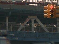 A telephoto shot of the Manhattan bridge a subway train, pedestrians, and cars travel across.  A traffic light is in the foreground Stock Footage