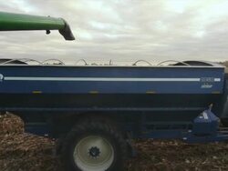 The auger from a combine empties corn into a wagon as both drive down the field harvesting. Stock Footage