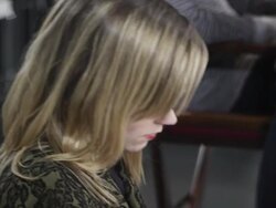 MS R/F PAN Female fashion model backstage at fashion show looking at smart phone then walking to sit in chair for hair stylist to style hair Stock Footage