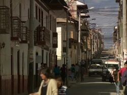 "View up busy side street, people milling around, man running, cars weaving past parked cars, balconys and electricity/phone/washing line cables criss-cross above, Plaza De La Armas, Chachapoyas, Peru [PerÃƒÂº]" Stock Footage