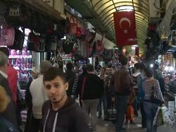 Shoppers mill through souk in Antakya Turkey with Turkish flag hanging from rafters Stock Footage