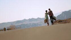 Young couple in love stroll together up sweltering desert road Stock Footage