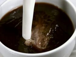 CU SLO MO Milk pouring into bowl of coffee against white background / Vieux Pont, Normandy, France  Stock Footage