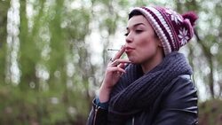 A chic adolescent girl with a funny cap enjoying smoking a cigarette Stock Footage