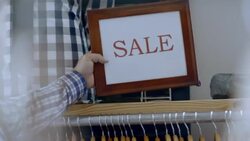 Small business employee places SALE sign on shelf above shirt rack in local clothing store Stock Footage