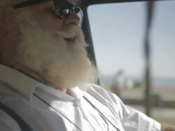 M/S big man w/ white long hair (Santa Claus), beard and moustache, sunglasses, driving and singing, background of palms Stock Footage