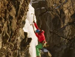 MS ZO PAN SLO MO Shot of ice climber climbing steep pillar of ice with ice shatters as climber hits with his pick and snow falling from above / Cody, Wyoming, United States Stock Footage