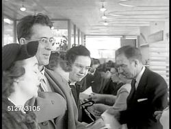 1953: LEVITTOWN, PENNSYLVANIA: SALES CENTER: Busy counter, couple in FG picking location of home, signing papers. Instructional Video