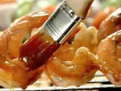 ECU basting brush adds second layer of barbecue sauce over shrimp on skewers on open flame grill Stock Footage