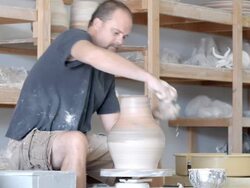 MS potter in pottery studio at pottery wheel dips sponge into water cup and presses wet sponge against spinning vessel to shape its neck   / Palm Springs, California, USA Stock Footage
