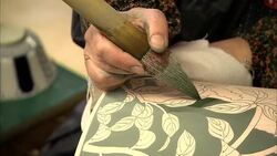 An artist paints green glaze onto a ceramic vase. Stock Footage