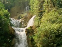 MS SLO MO Shot of waterfall between green vegetation and brown rocks / Kuang Si, Luang Prabang, Laos Stock Footage