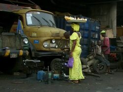 MS Shot of woman in bright yellow dress passes by men servicing old lorry under motorway bridge / Lagos, Nigeria Stock Footage