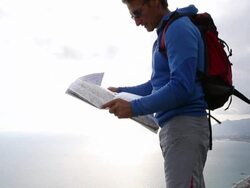 Pan up, hiker looks at map on cliff above sea Stock Footage