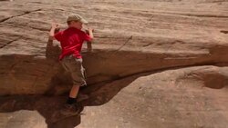 Camera follows young hiker boy scaling the side of a rocky canyon wall Stock Footage