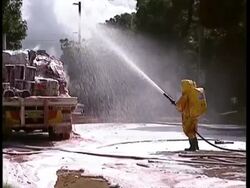 MS Fire fighter in chemical suit hosing down chemicals with foam Stock Footage