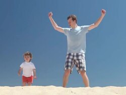 Personal trainer  - father and son do star jumps on the beach Stock Footage