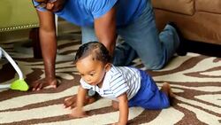 MS Father helping infant son crawl on floor in living room Stock Footage