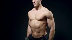 beautiful athlete trains with a dumbbell on a black background Stock Footage
