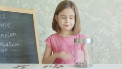 Girl looks at list of life plans on chalkboard then puts coins in glass jar Stock Footage