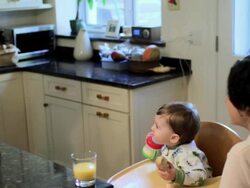 Baby boy sitting in high chair eating breakfast with parents Stock Footage
