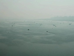 A single motorized riverboat leaves it's wake in the vast expanse of Mother Ganga, tiny rowing boats dotted about on silvery surface. India Stock Footage