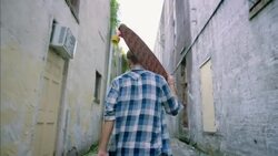 Young man walks through downtown alley carrying custom wooden longboard Stock Footage