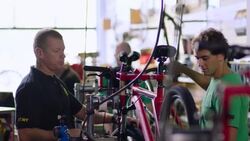 Boss chats with young mechanic working on bicycle in bike shop Stock Footage