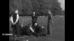 1937: BERLIN, NAZI GERMANY: WS People relaxing on park grass. Men in suits sitting on grass, playing cards. AMUSEMENT RIDE: Adults looking upward. Children in round roller coaster car. MS Children, adults looking (R). Instructional Video