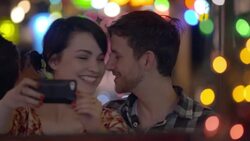 Young woman takes a selfie with smartphone as boyfriend kisses her cheek Stock Footage