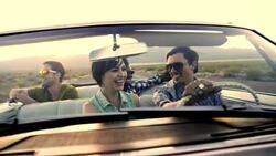 Group of friends drive up lonely desert road in classic convertible Stock Footage