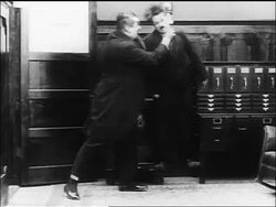 B/W 1916 Charlie Chaplin trying to scratch leg while being held in air by large man (Eric Campbell) Stock Footage