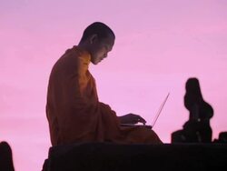 WS A Buddhist monk types on a laptop computer on top of an ancient temple at sunrise in Angkor Wat / Siem Reap, Cambodia Stock Footage