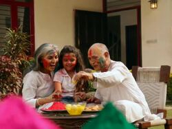 Senior man feeding rasgulla to his granddaughter in holi festival  Stock Footage