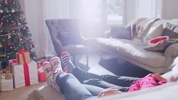 Affectionate couple relaxing in socks with feet up on sofa facing Christmas tree Stock Footage