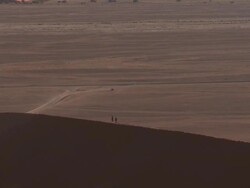Two people walking on sand dune, vehicle in distance, Sossusvlei, Namib-Naukluft, Namibia Stock Footage