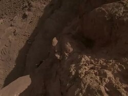 Medium Long Shot crane - A rugged cliff casts giant shadows upon distant rock climbers that scale its face / Morocco Stock Footage