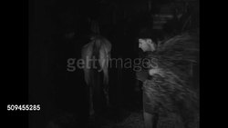 1912 DRAMATIZATION: NIGHT: Men waiting by firebox. EXT Stable w/ Fire Marshal walking next to building. Arsonists setting up barn to burn, moving hay near old horses, investigators waiting outside, men exiting barn. Male lighting candle in barn. Instructional Video