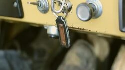 Road Trip keychain hangs in ignition as man in boots pumps clutch and accelerates in classic yellow Ford Bronco Stock Footage