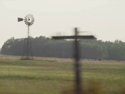 Driving by a windmill partially obscured by trees in the foreground Stock Footage