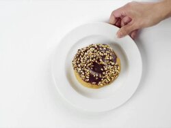 CU Woman hand entering setting down round white plate with large donut with chocolate frosting and nuts / Omaha, Nebraska, United States Stock Footage