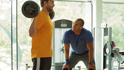 Personal trainer guiding man doing barbell squats at gym Stock Footage