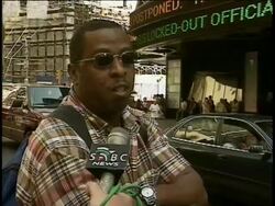 9/11/01-- SABC interview hours after attack w/ West Indian Black man wearing sunglasses in Times Square; describes his horrified & saddened reaction. News headlines run on zipper screen in BG. Stock Footage